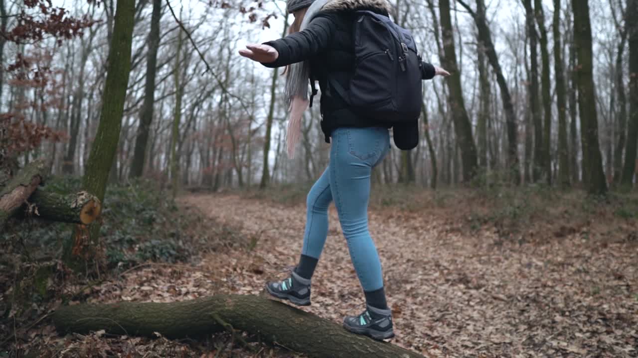 Young female caucasian photographer walking and balancing on cut tree laying on leaf covered road in forest, SLOW MOTION