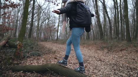 young female caucasian photographer walking and balancing on cut tree laying on leaf covered road in forest, slow motion