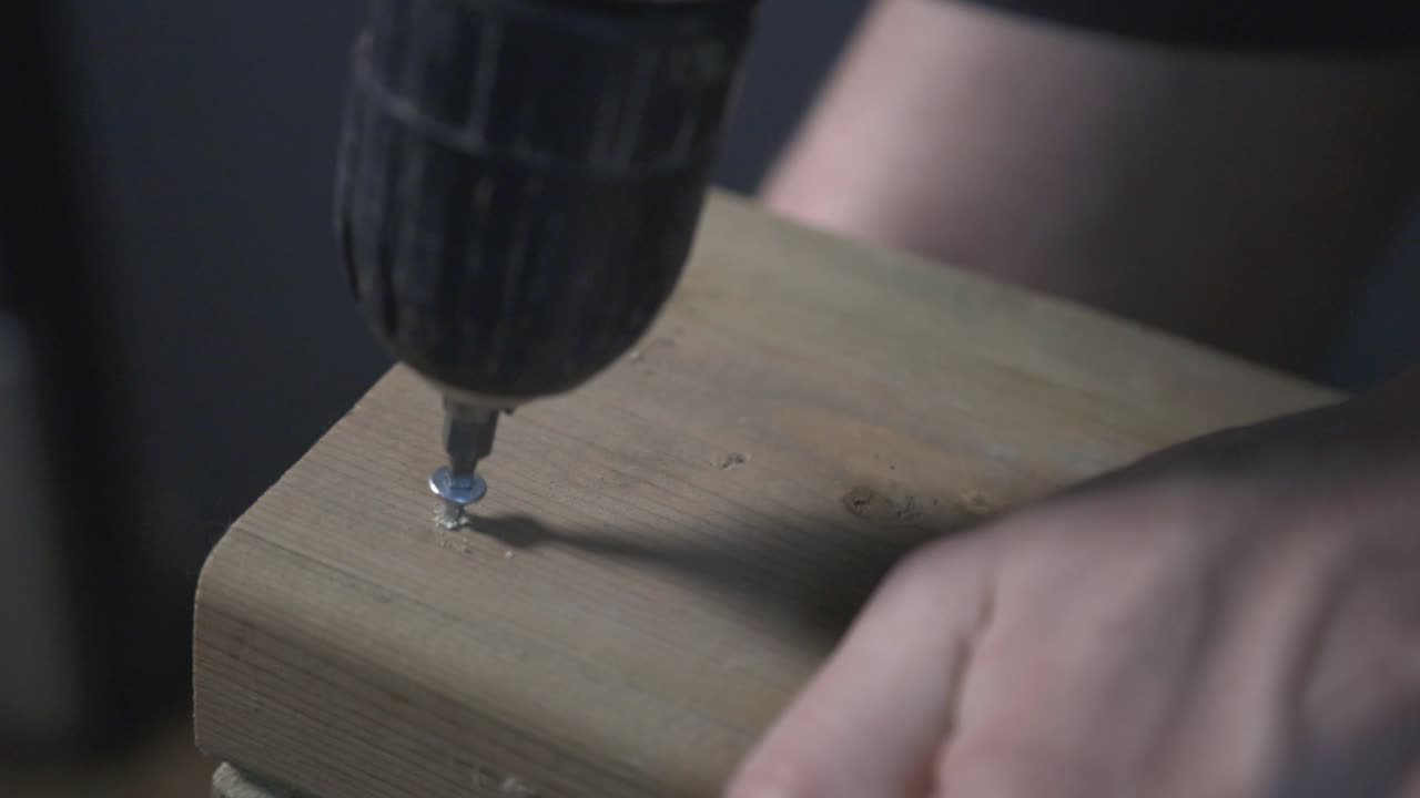 Hands Of A Carpenter Doing Woodwork In The Workshop. Drilling Screw On A Wooden Board. - close up shot