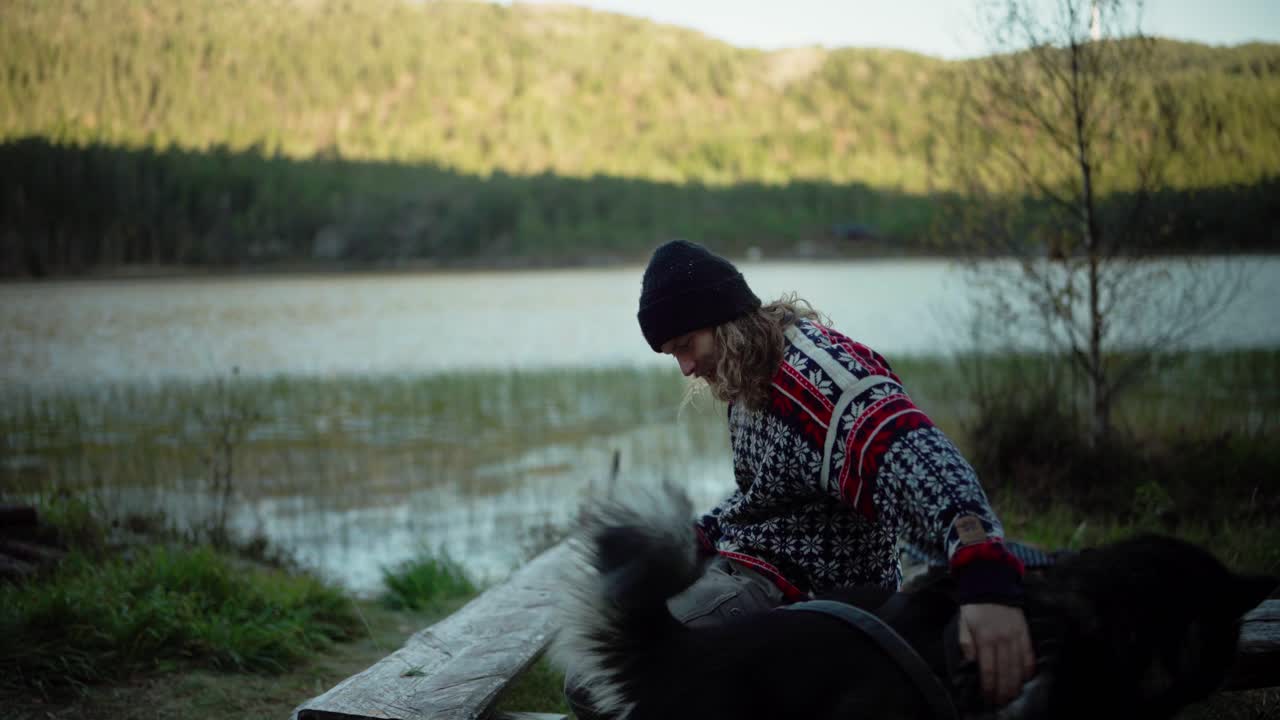 hildremsvatnet, trondelag, noruega - un hombre disfruta de una bebida caliente mientras acaricia a su perro - de cerca