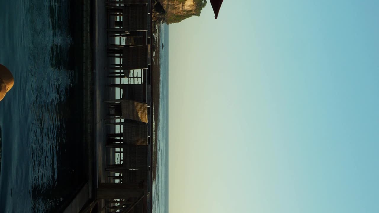 Vertical Ascending shot from an infinity pool above suluban beach during low tide while a model in a sun hat swims on a sunny summer day
