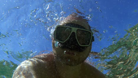 un hombre con máscara de buceo en agua de mar clara se divierte con burbujas de aire submarinas de la boca durante las vacaciones de verano