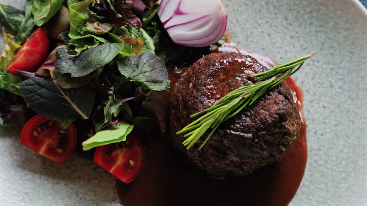 Close up of a filet mignon with a red wine sauce and a fresh salad garnish