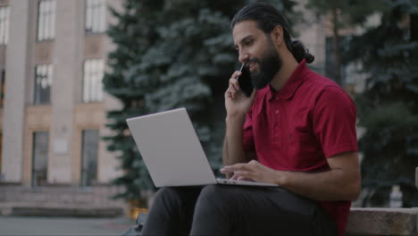 hombre trabajando en una computadora portátil y hablando por teléfono al aire libre