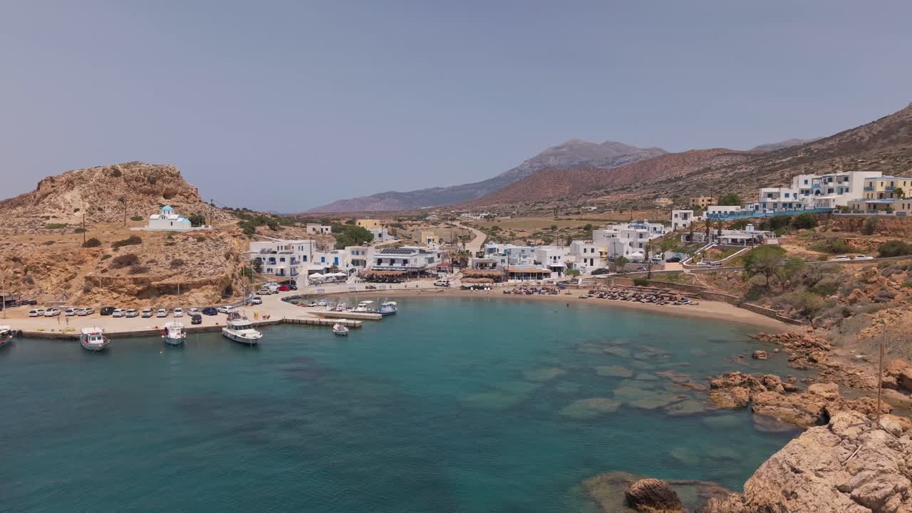 Drone ascending to the sky reveals the traditional Finiki fishing village in Karpathos with its harbor, boats, and stunning Mediterranean coastline