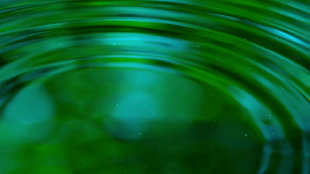 Zeitlupenaufnahme von Wassertropfen, die Wellen auf einer grünen Flüssigkeitsoberfläche erzeugen