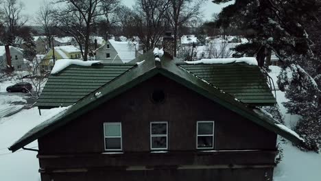 snowy push in of cabin in suburban neighborhood drone shot