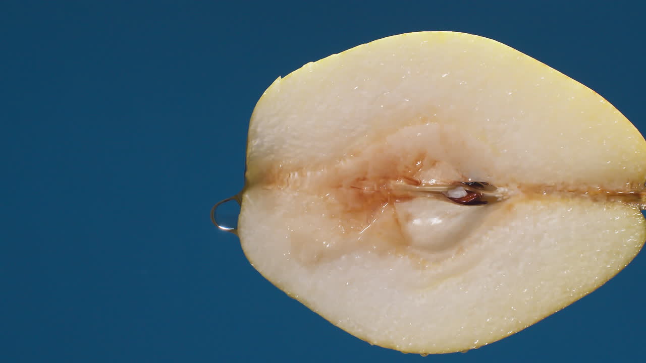 Vertical yellow half pear on a blue dark background with drops of water rolling down the pear and flowing splashing with isolated background