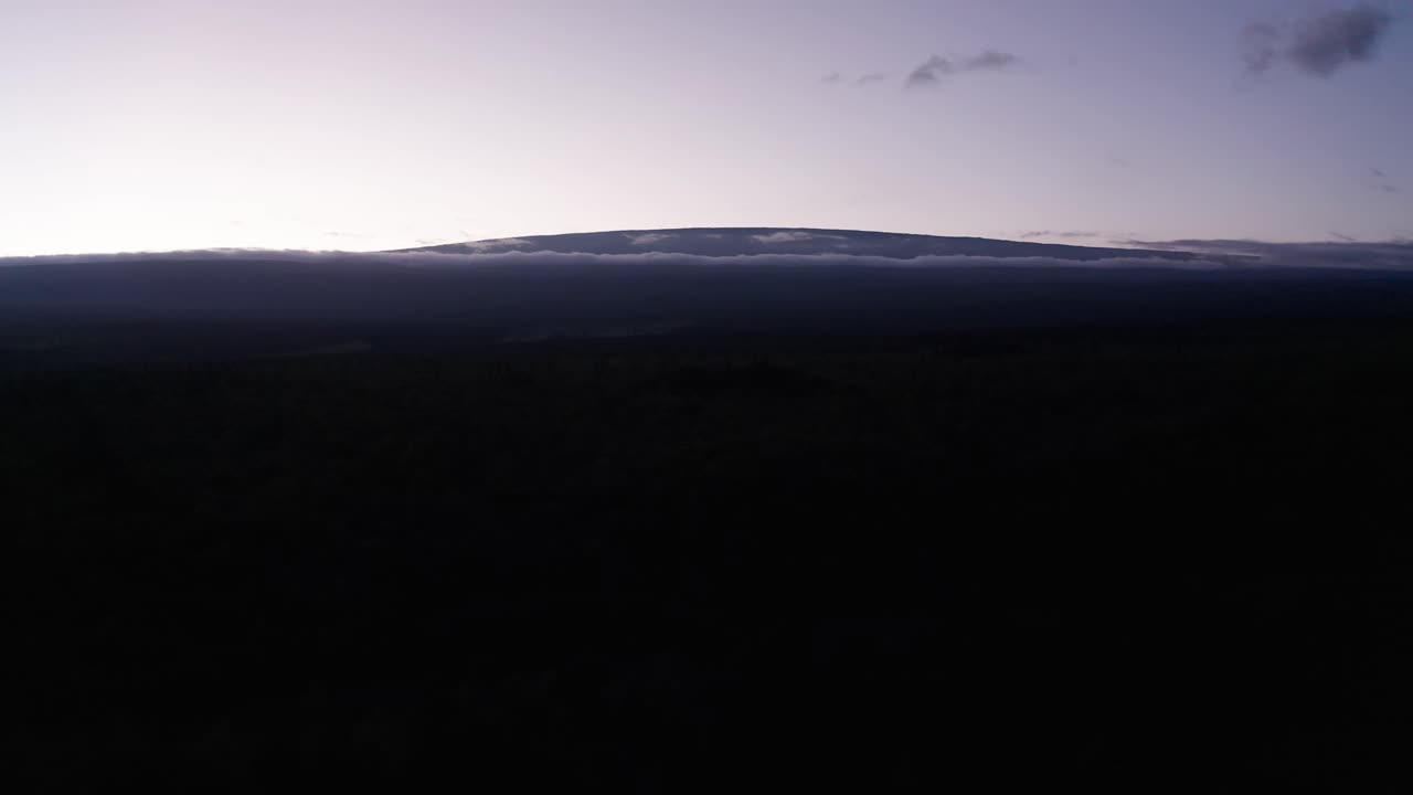 Aerial reverse pullback descending shot of Mauna Loa towering above the clouds at sunset in Hawai'i