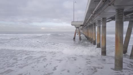 volando bajo el muelle de venecia hacia un lado sobre el océano para ver a los surfistas en el agua