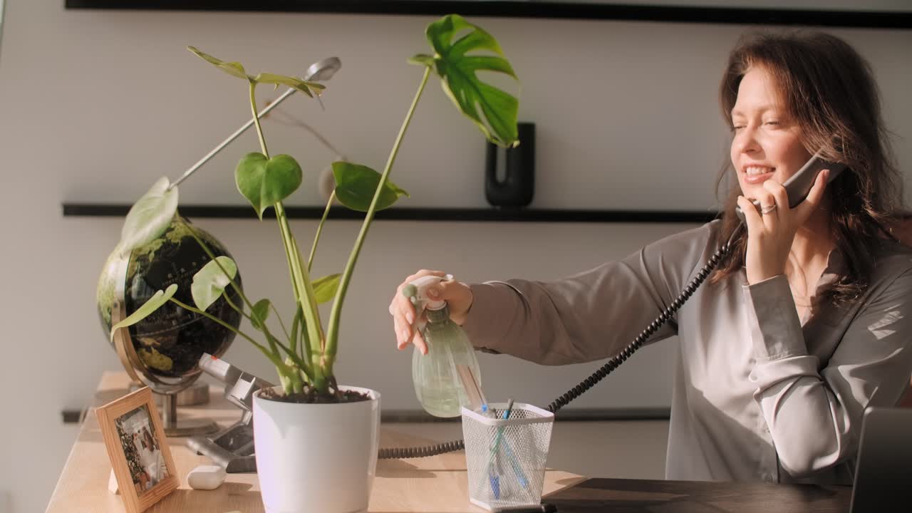 Woman Watering Plant and Talking on Phone in Home Office