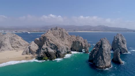 wide shot aerial drone view of rock formations with a natural arch formation located on the beach