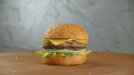 In-slow-motion-sesame-seeds-fall-on-a-spinning-hamburger.-Hamburger-on-a-wooden-Board