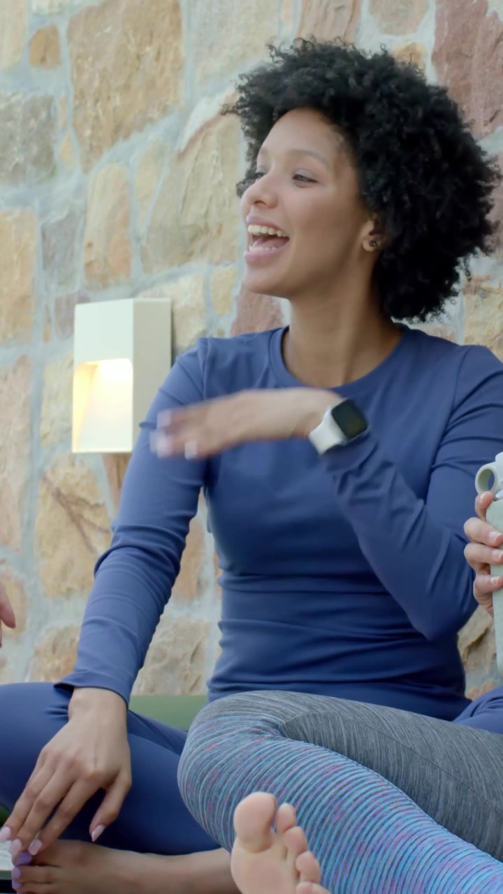 Video verticale: Sentendo una voce a sinistra, donna con top blu che parla in veranda durante una pausa, indossando uno smartwatch.