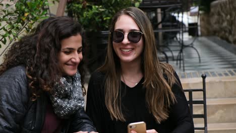 two happy friends looking at a smartphone together outdoors