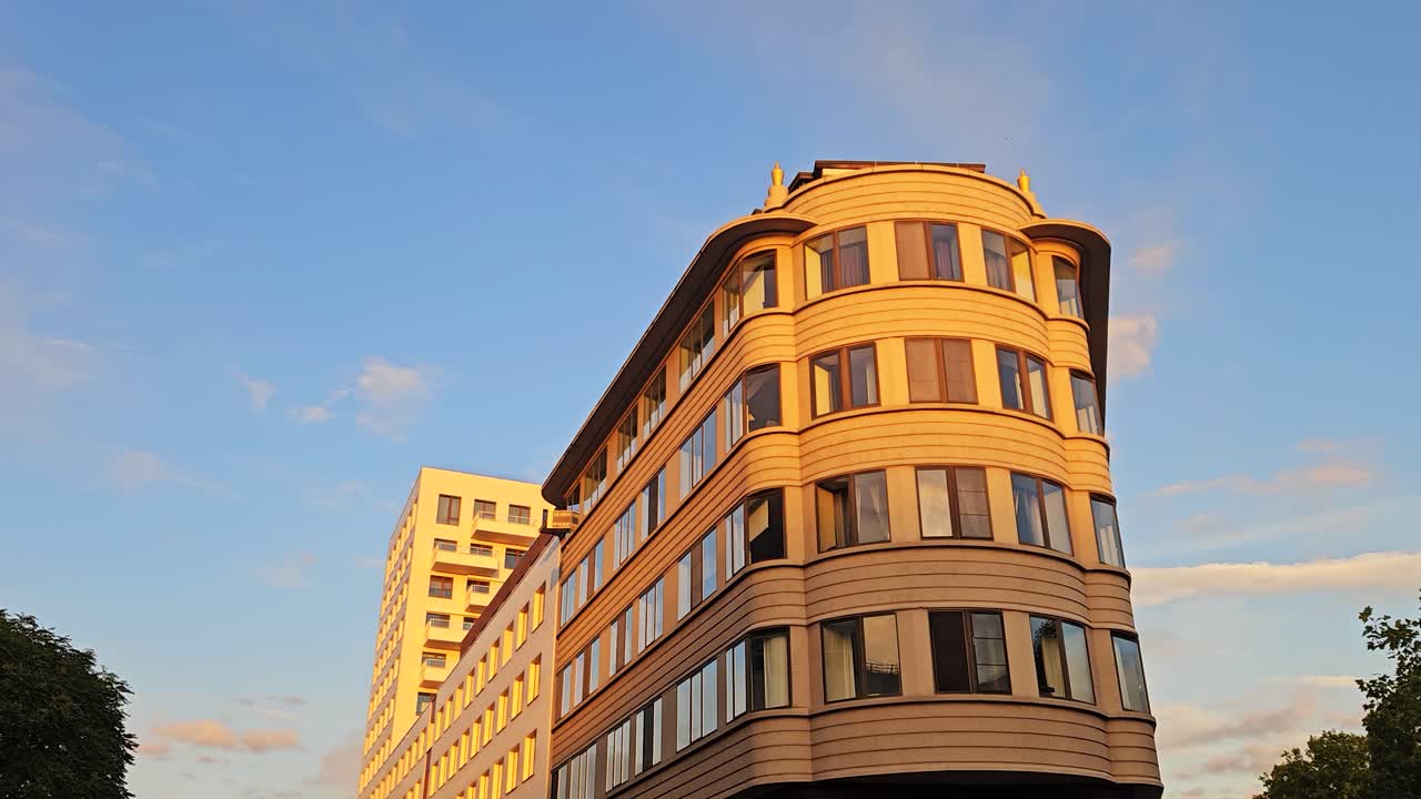 Walking shot of a curved corner apartment building in warm sunset light with golden reflections on the windows