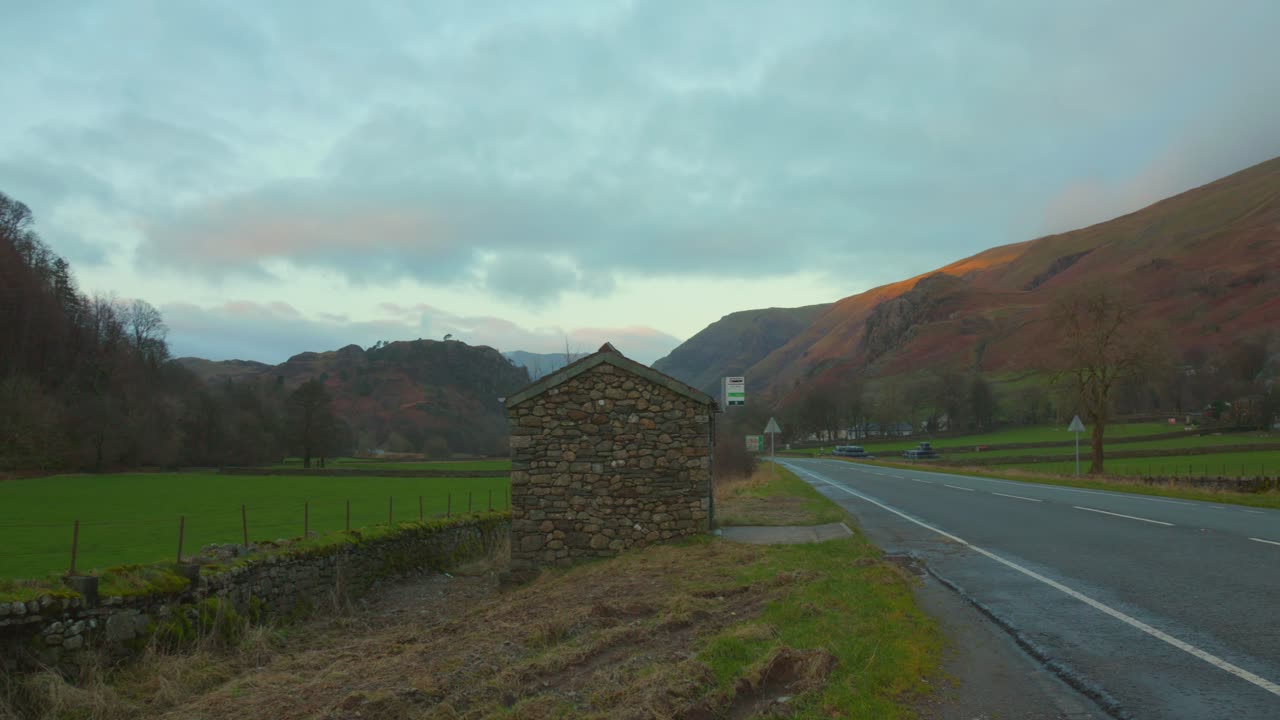 cobertizo de piedra por el camino del campo con coches en inglaterra en un día nublado