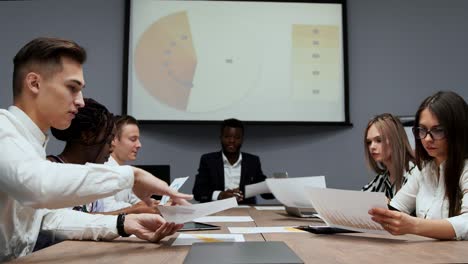 a group of creative multi-ethnic managers disassemble at the meeting of the board of directors in the conference hall the graphs of profit for the last year in the firm. the boss of an african american and a multi-ethnic creative office team discuss the