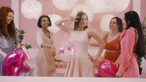 front view of a happy bachelor girl with headdress and veil dancing at camera with her friends