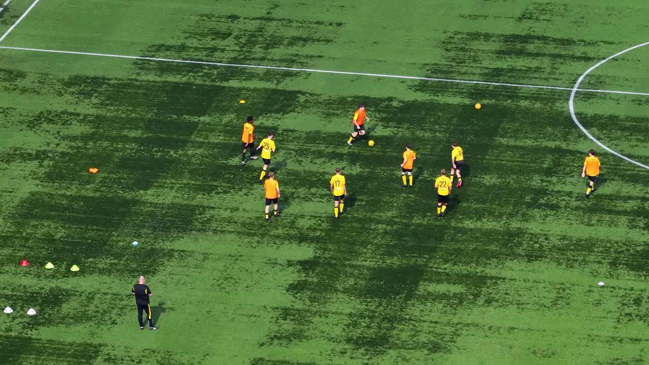 Aerial view of youth soccer players practicing drills on green grass pitch under daylight