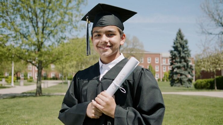 Adolescente diplomato che festeggia, tenendo in mano un diploma arrotolato nel cortile universitario, mentre la telecamera si avvicina, in tocco e toga.