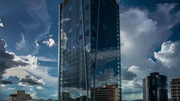 Torre di vetro riflettente che mostra nuvole in movimento sul tetto, con nuvole che passano creando effetti dinamici.