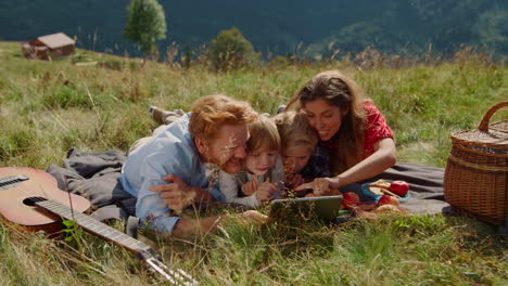 family holding tablet picnic lying grass mountain hill. people using tab outdoor