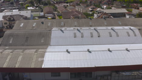 Panoramic aerial shot captured by drone showing a mixed landscape of homes, factory roofs, mountains in the background, and extensive green areas.