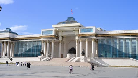 establishing shot of the government palace in sukhbaatar square, ulaanbaatar, mongolia, featuring the towering mongolian flag and the genghis khan statue placed at its front center.