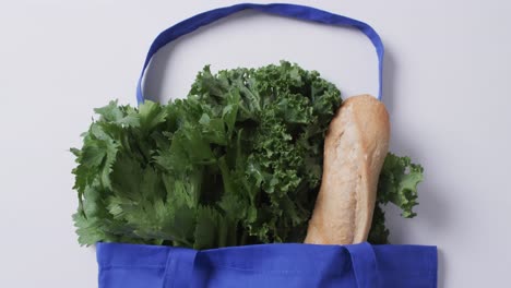 Video-of-blue-canvas-bag-with-parsley,-kale-and-baguette,-copy-space-on-white-background
