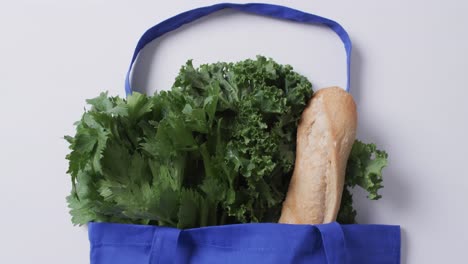 video de una bolsa de lienzo azul con perejil, col rizada y baguette, copia espacio en fondo blanco