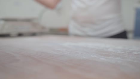 disparo en cámara lenta de un panadero artesano rociando harina en una mesa de madera rústica para preparar pan
