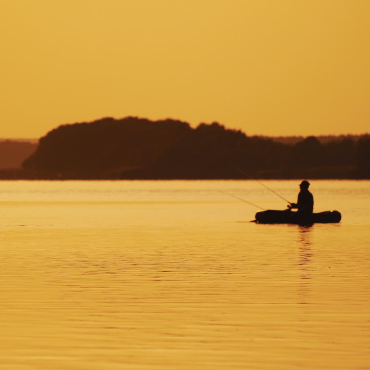Golden sunset and the silhouette of a man throwing a fishing rod from the boat. Fisherman is catching fish from a rowboat in the evening on the background of natural landscape.