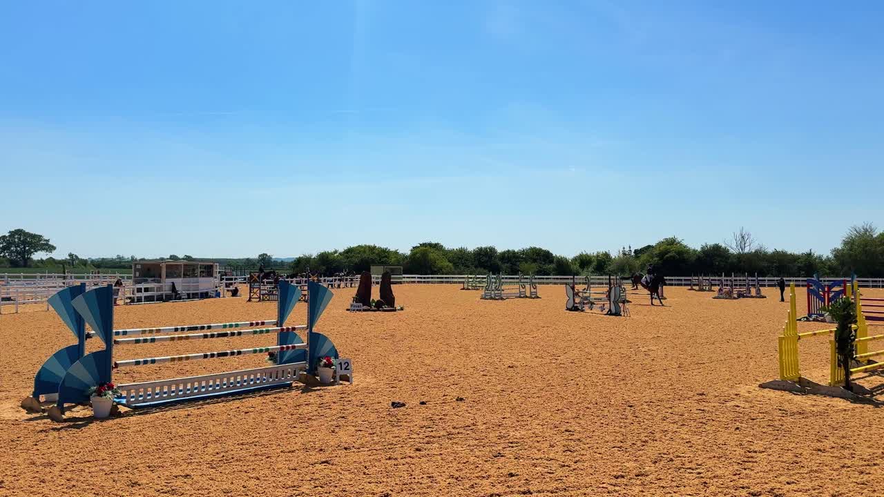 Outdoor Horse Jumping Arena with Jumps and Riders Under a Clear Sky