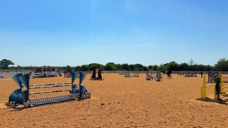 outdoor horse jumping arena with jumps and riders under a clear sky