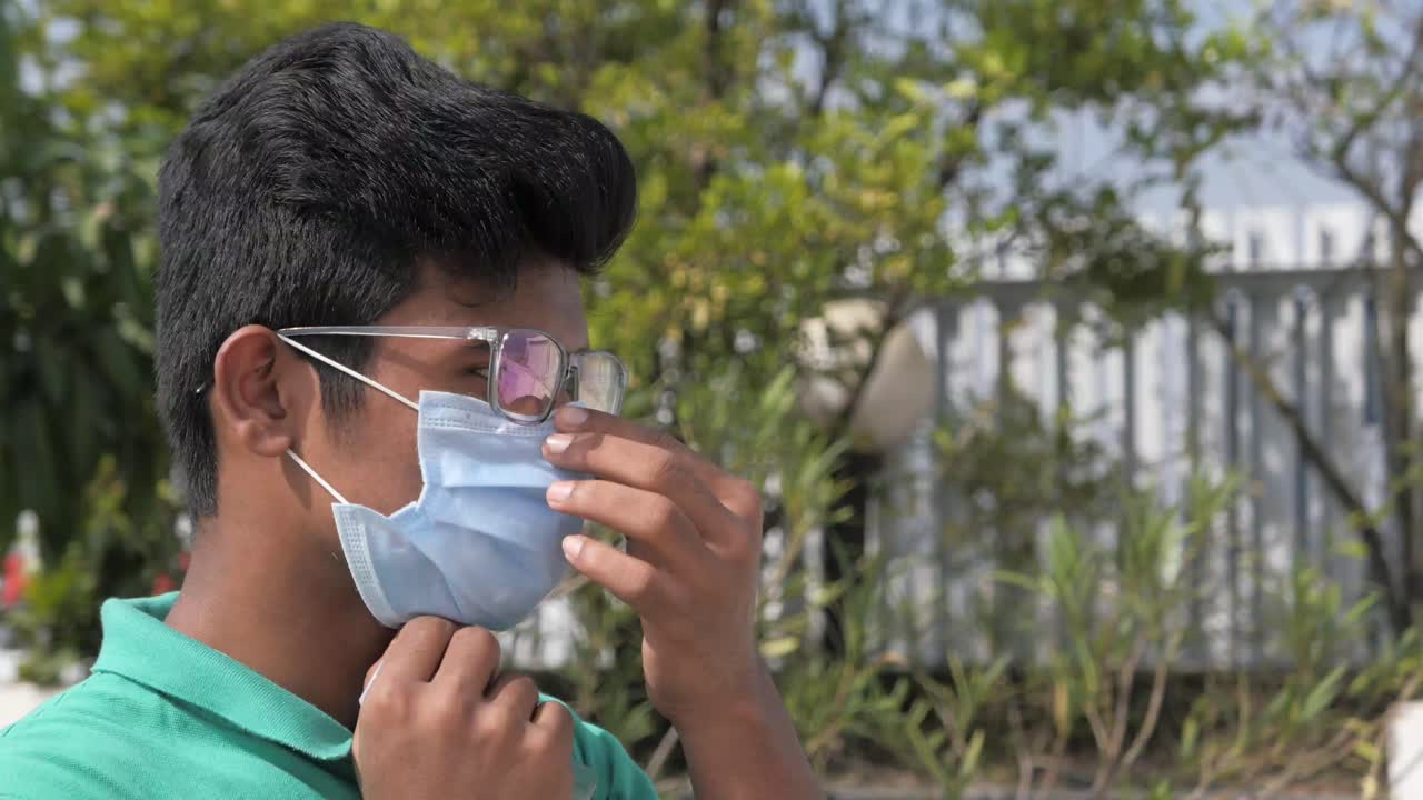 젊은이가 야외에서 얼굴 마스크를 조정하고 있습니다.