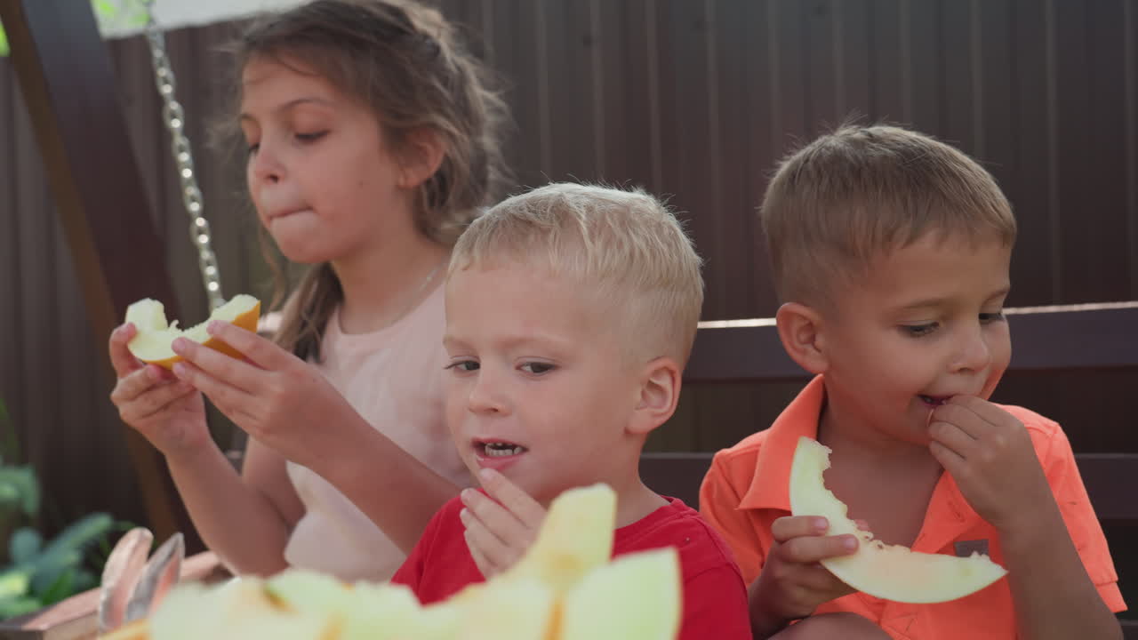 Caucasian Children Tasting Melon On Wooden Swing Bench, Three Kids Sampling Slices With Varied Expressions, Juicy Bites, Bright Summer Lighting, Playful Sharing And Messy Enjoyment