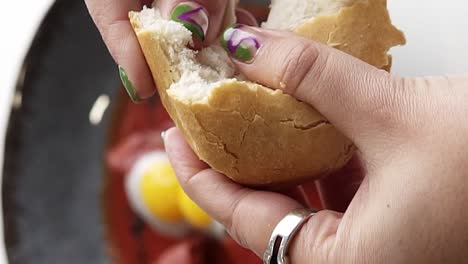 woman's gentle hand dipping bite of bread into eggs and tomato sauce