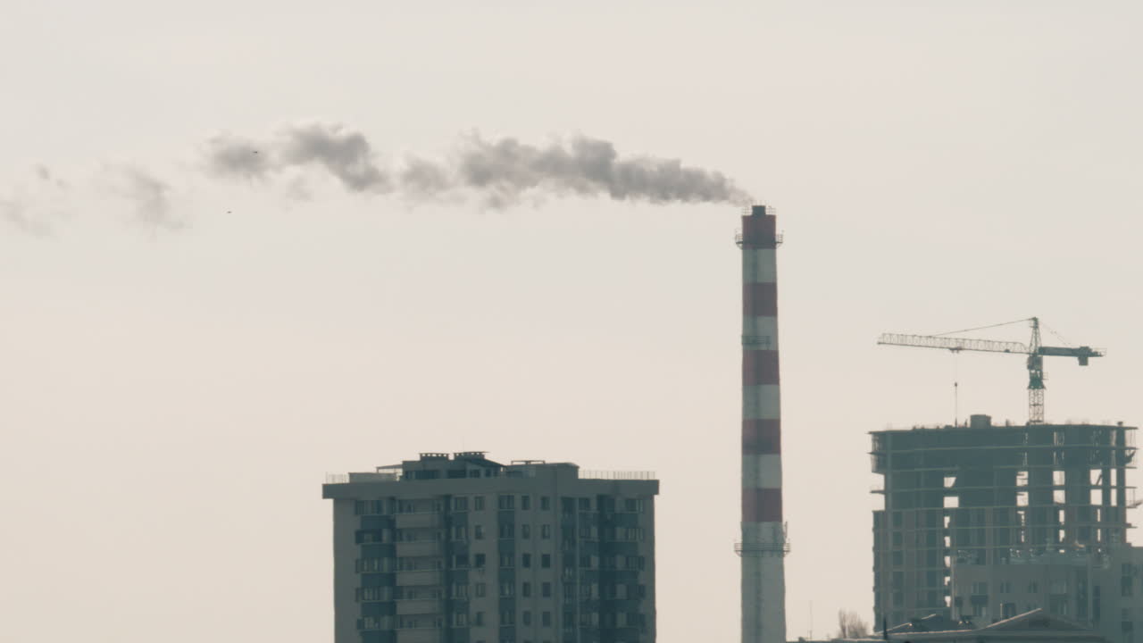 Urban skyline with residential buildings and an industrial chimney emitting smoke at sunset