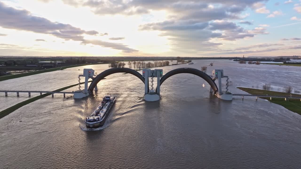 Aerial orbit drone shot to the right at the weir of Driel during high water levels with the doors open and a ship passing thru the weir