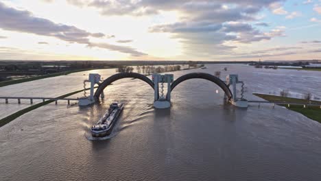 aerial orbit drone shot to the right at the weir of driel during high water levels with the doors open and a ship passing thru the weir