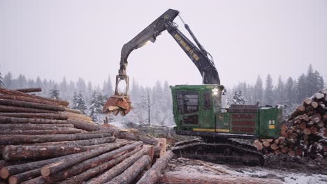 Industrial timber manipulator logging machine sorting piles of wood in snowstorm