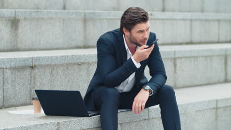 Businessman-talking-on-phone-loudspeaker-in-city.-Man-using-mobile-phone