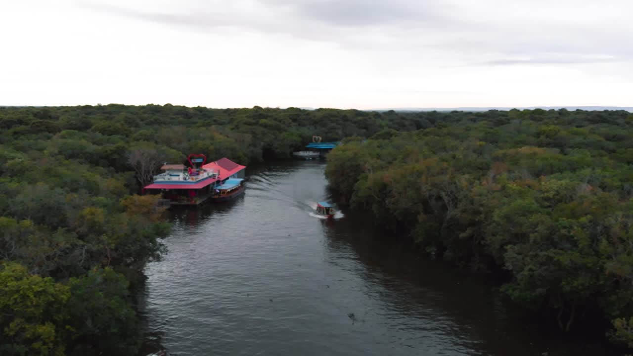 An aerial drone shot over a partially submerged forest in Cambodia, with small boats navigating through the trees, showcasing the region's unique seasonal flooding and natural beauty.