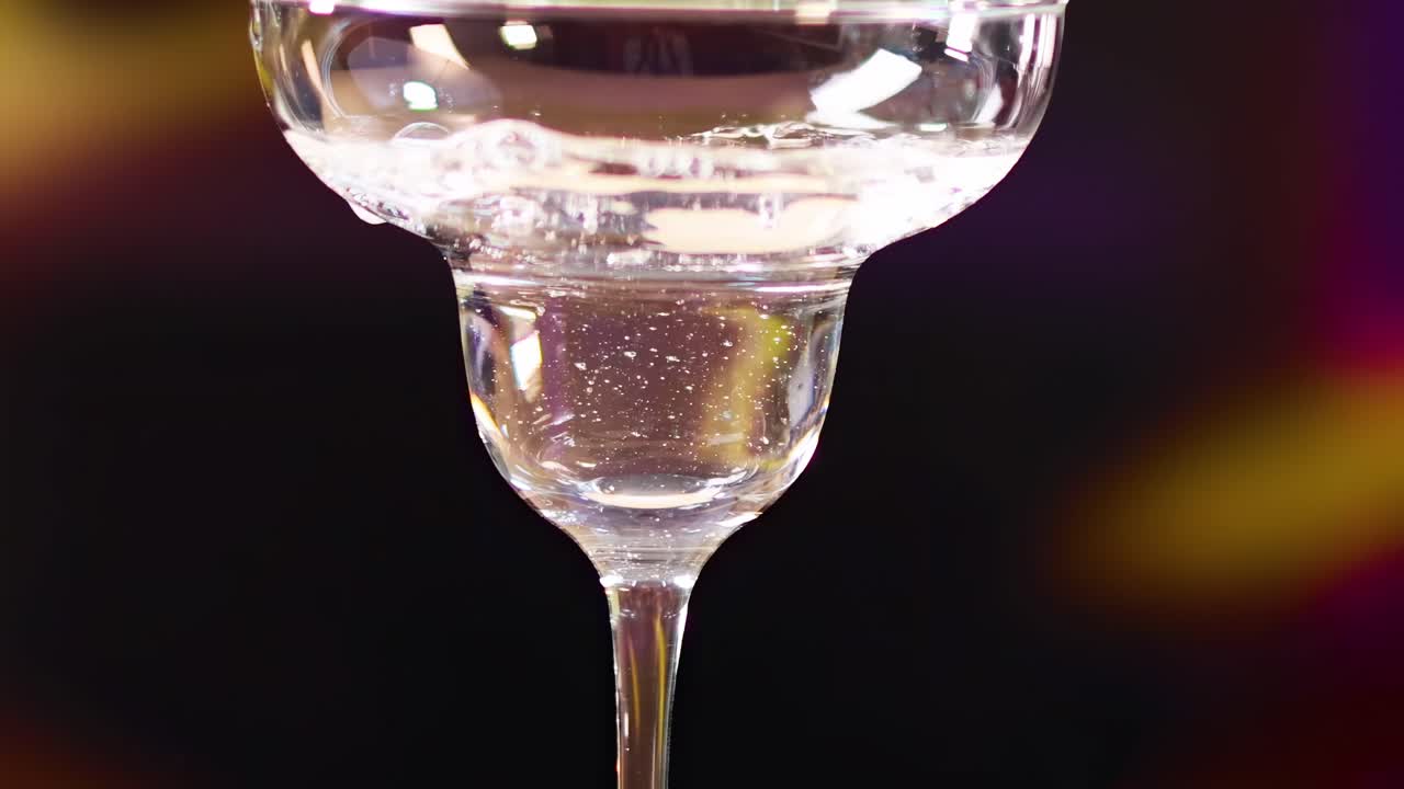 A close-up sequence of olives on a skewer being placed into a martini glass with a colorful background.