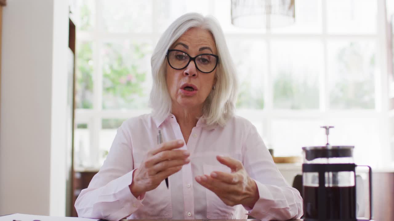 Portrait of senior woman wearing glasses talking looking at the camera while working from home