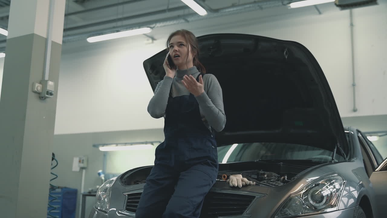 Mechanic female using a smartphone having a call in a car workshop. International Women's Day.