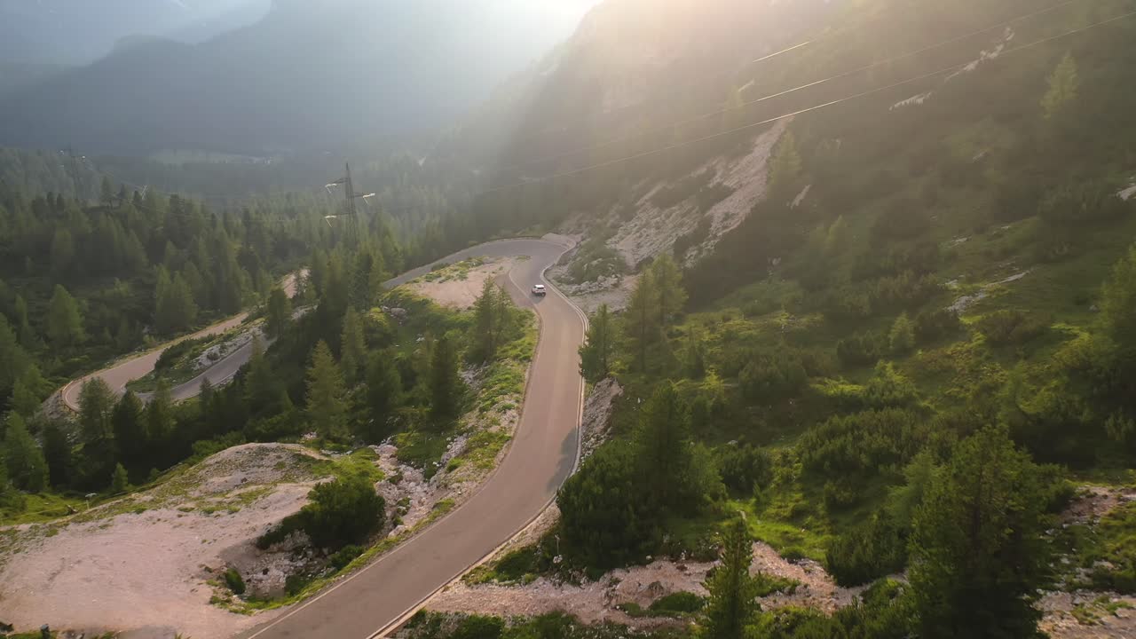 White car driving down winding mountain road in Italy, tilt up aerial