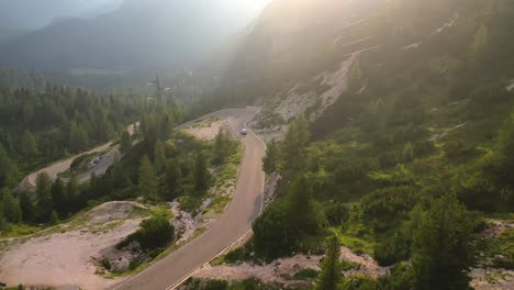white car driving down winding mountain road in italy, tilt up aerial