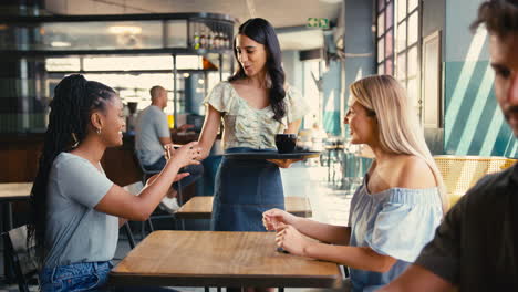 mujer en una cafetería conociendo a un amigo pagando una factura con un teléfono móvil sin contacto